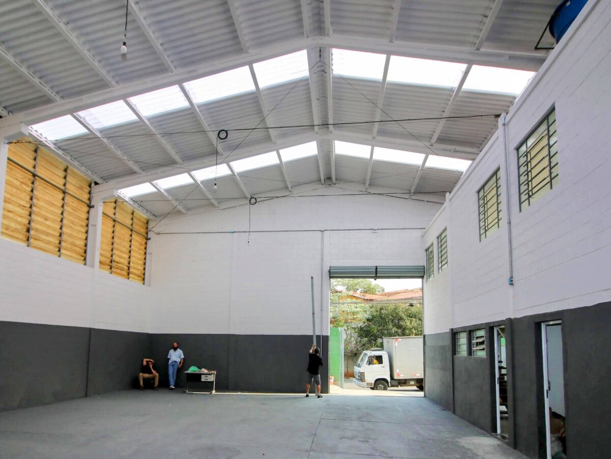 Vista interna do galpão recém pintado, com faixa escura na parte inferior de suas paredes e grade portão para acesso ao seu interior.