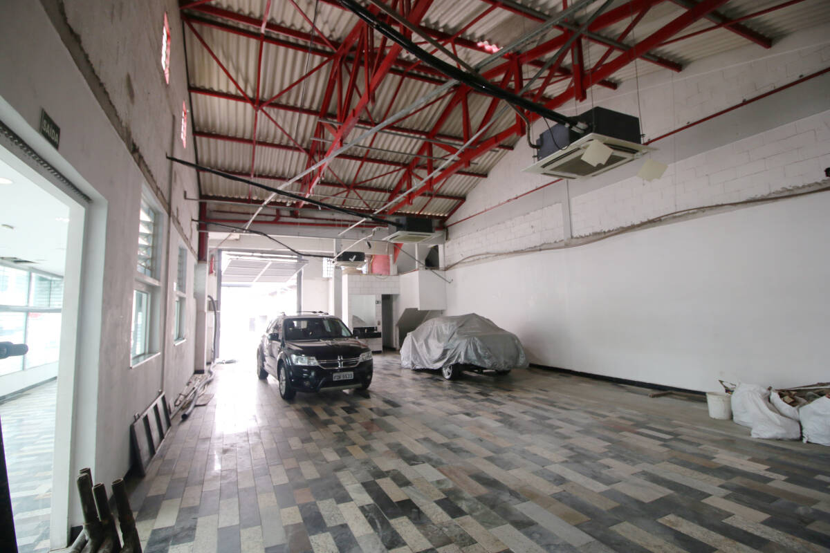 Vista interna de pequeno galpão, com 2 carros em seu interior.