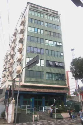 Edifício com 7 andares com fachada em ladrilhos verdes e esquadrias de vidro.